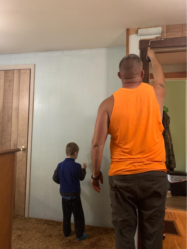 Allen Nanu of Al Paints rolling a doorframe in a Wayne County home while his young son paints the wall beside him